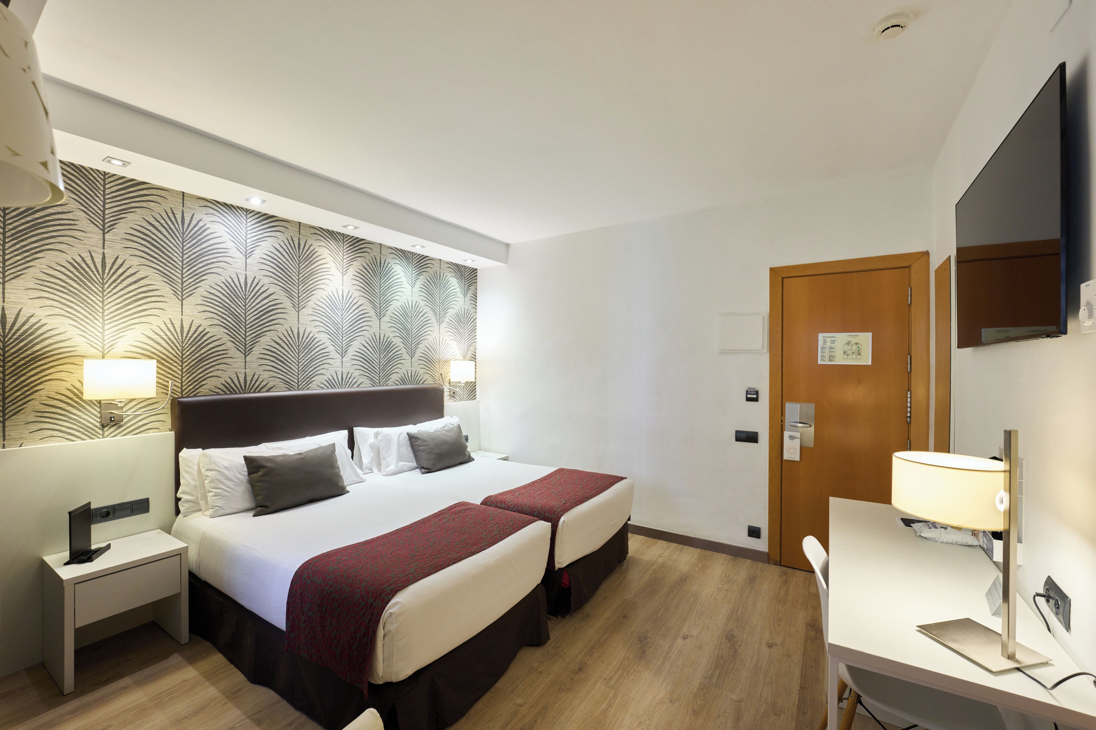 Ein Hotelzimmer mit einem Bett, zwei Nachttischen, einem Schreibtisch, einem Spiegel und einer Wand mit Muster.