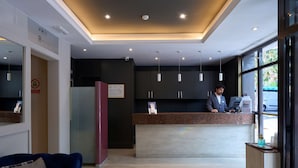 Zona de recepción de un hotel con mostrador, refrigerador, sofá azul y un ventanal grande.