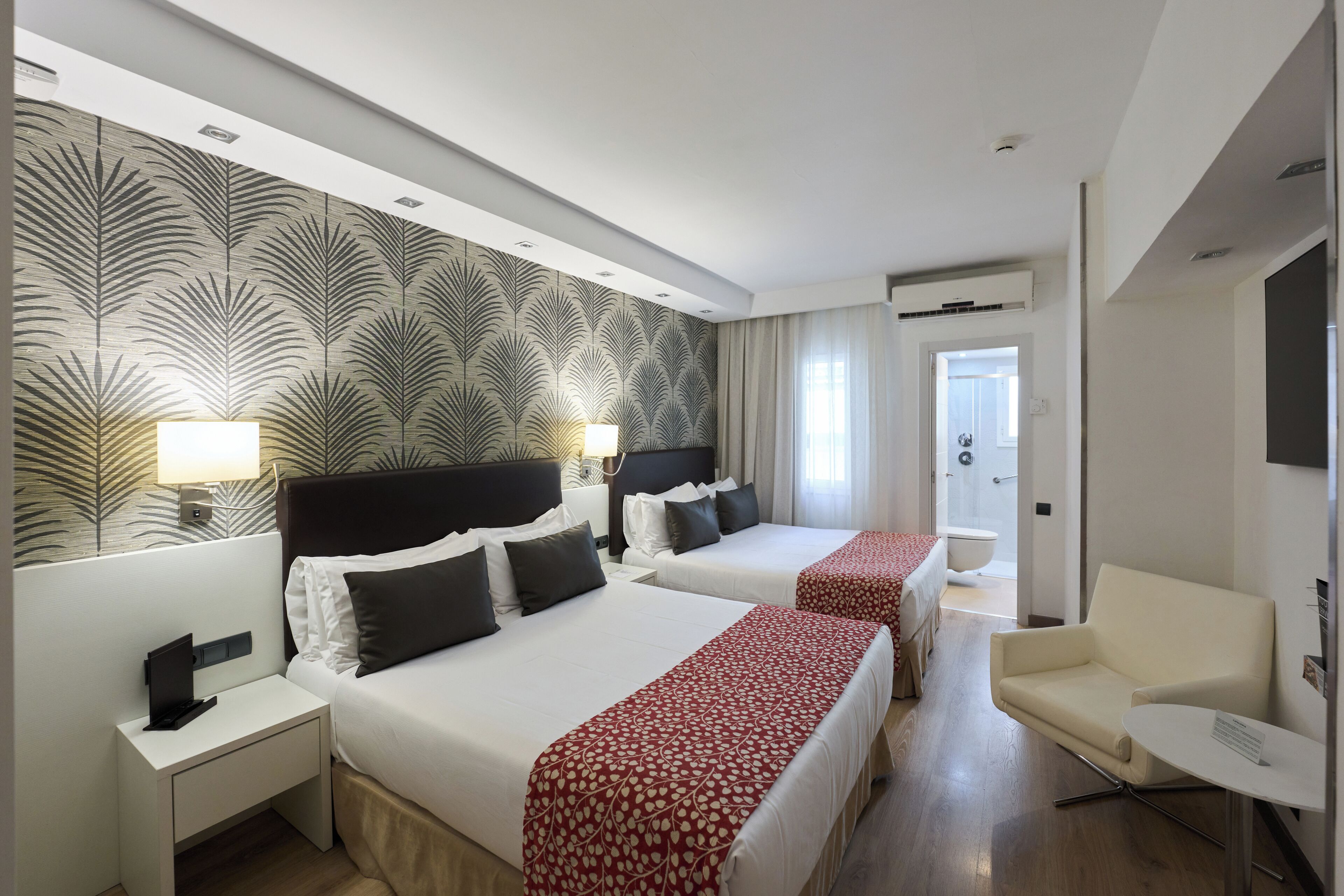Habitación de hotel con dos camas, un escritorio, una silla y un baño visible a través de una puerta abierta.