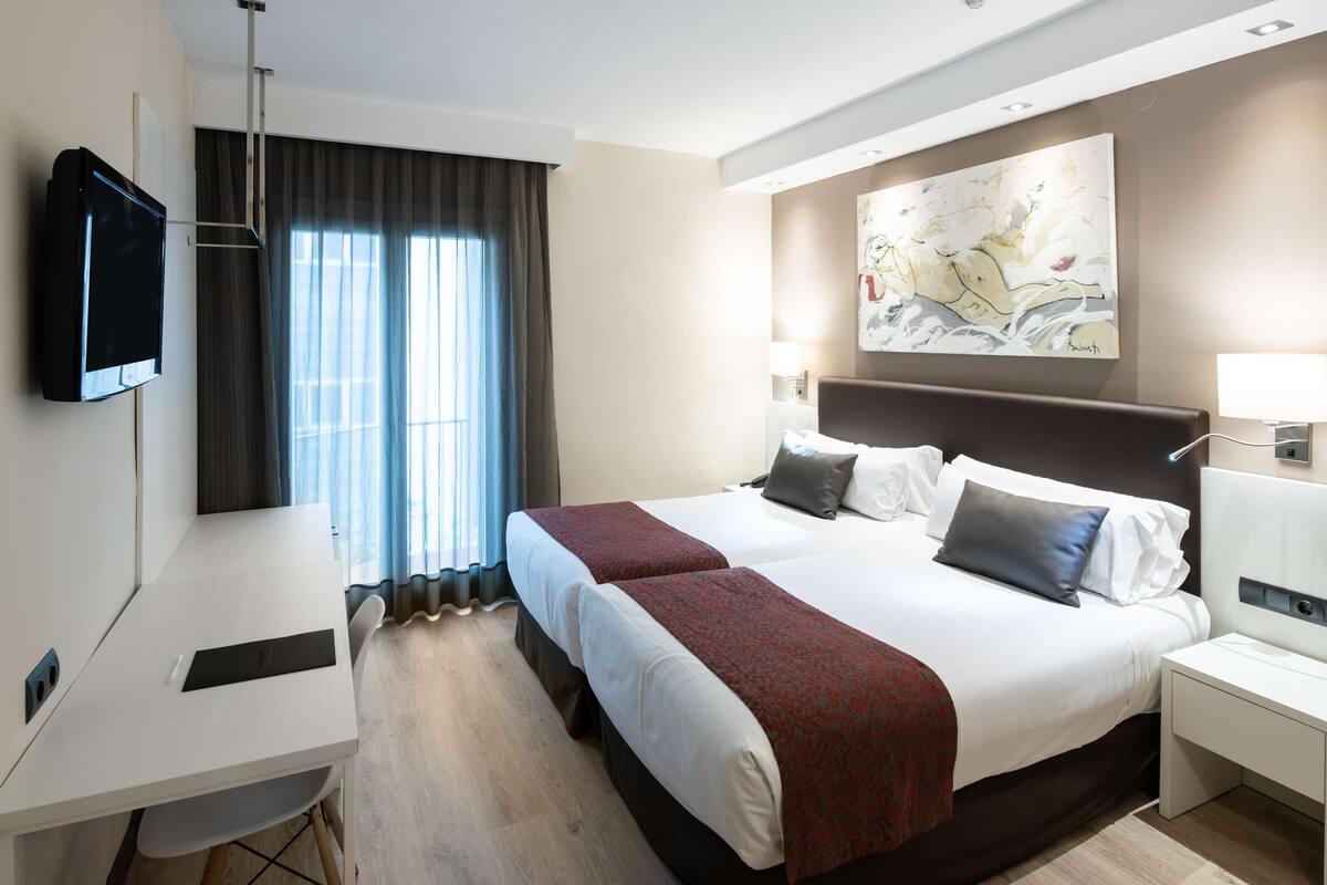 A hotel room with a large bed, a desk, a TV, and a painting on the wall.