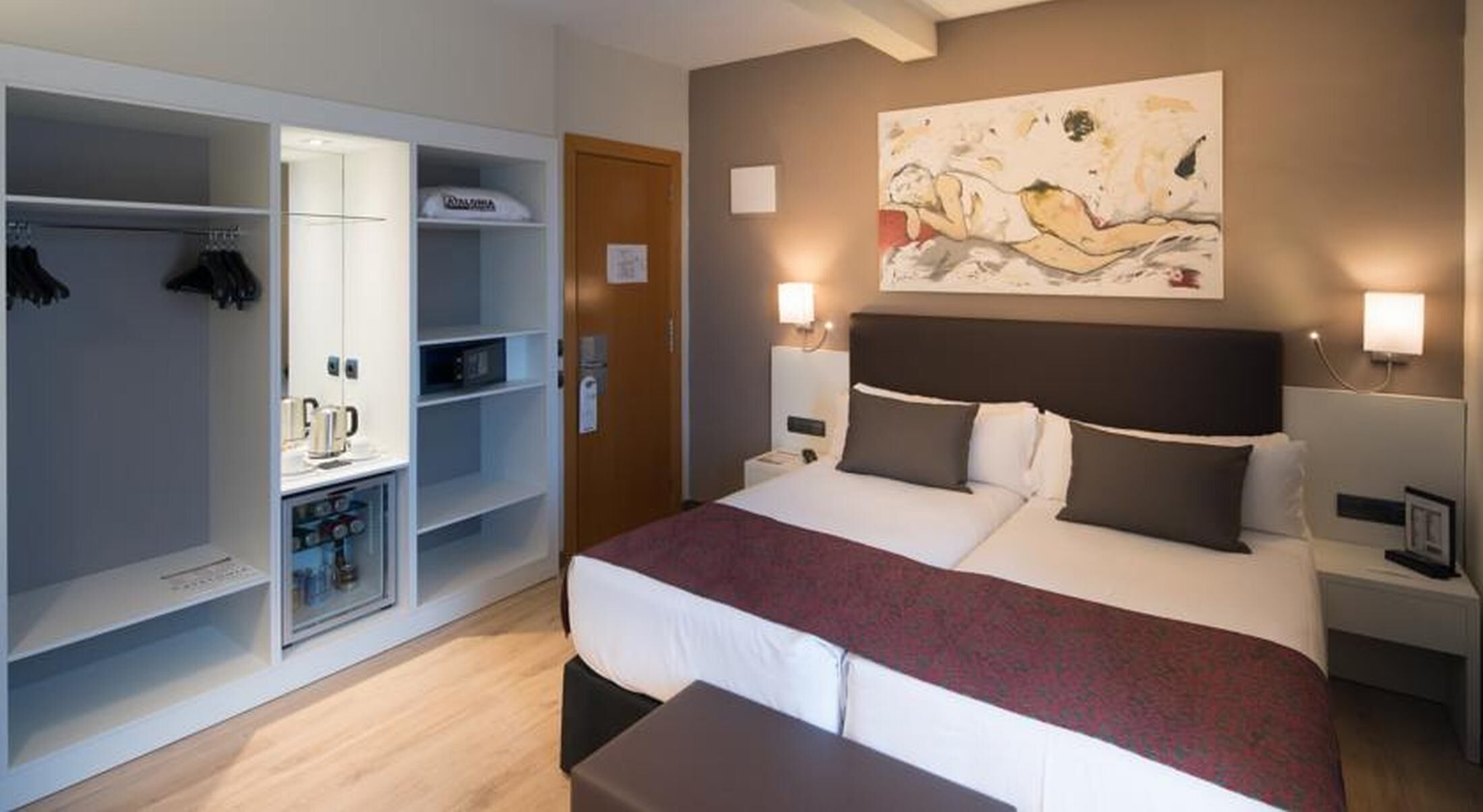 Et hotelværelse med seng, garderobeskab, minibar og et billede på væggen.