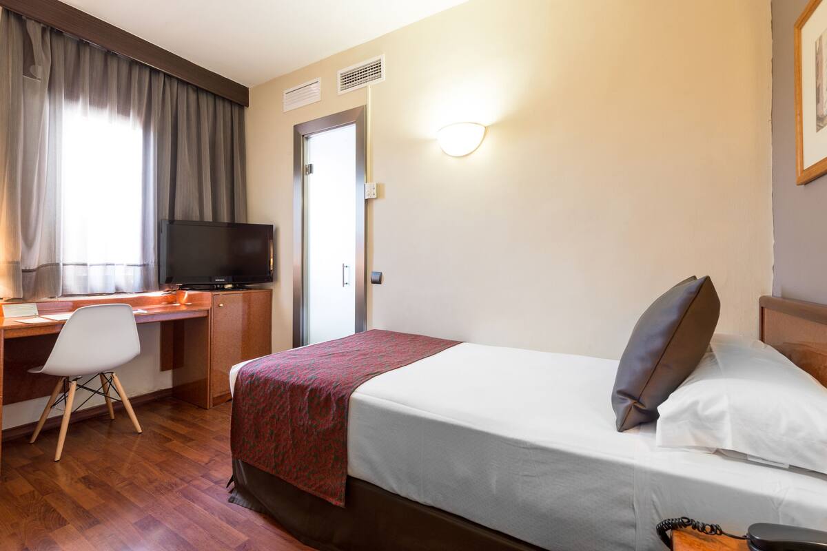 A hotel room with a bed, a desk with a computer, a chair, and a television.