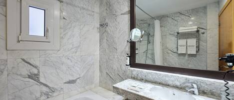 A bathroom with a marble wall, a bathtub, a large mirror, and a shower area.