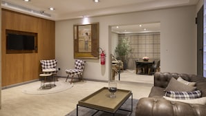Una sala de estar moderna con un sofá de cuero, sillones a cuadros, una mesa de centro y un cuadro en la pared.