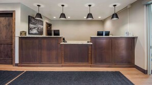 A reception area with a wooden reception desk, black pendant lights, a framed picture on the wall, and a sign above the desk.