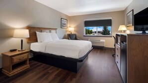 A hotel room with a bed, bedside lamps, a desk with a computer, a television, and a window with a view of trees and buildings.