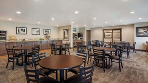 A hotel dining area with multiple round tables and chairs, a bar area, and framed pictures on the walls.