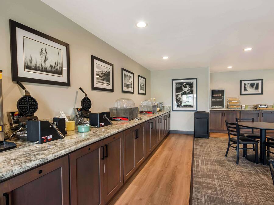 A modern kitchen with a marble countertop, coffee machines, and a dining area with a table and chairs.
