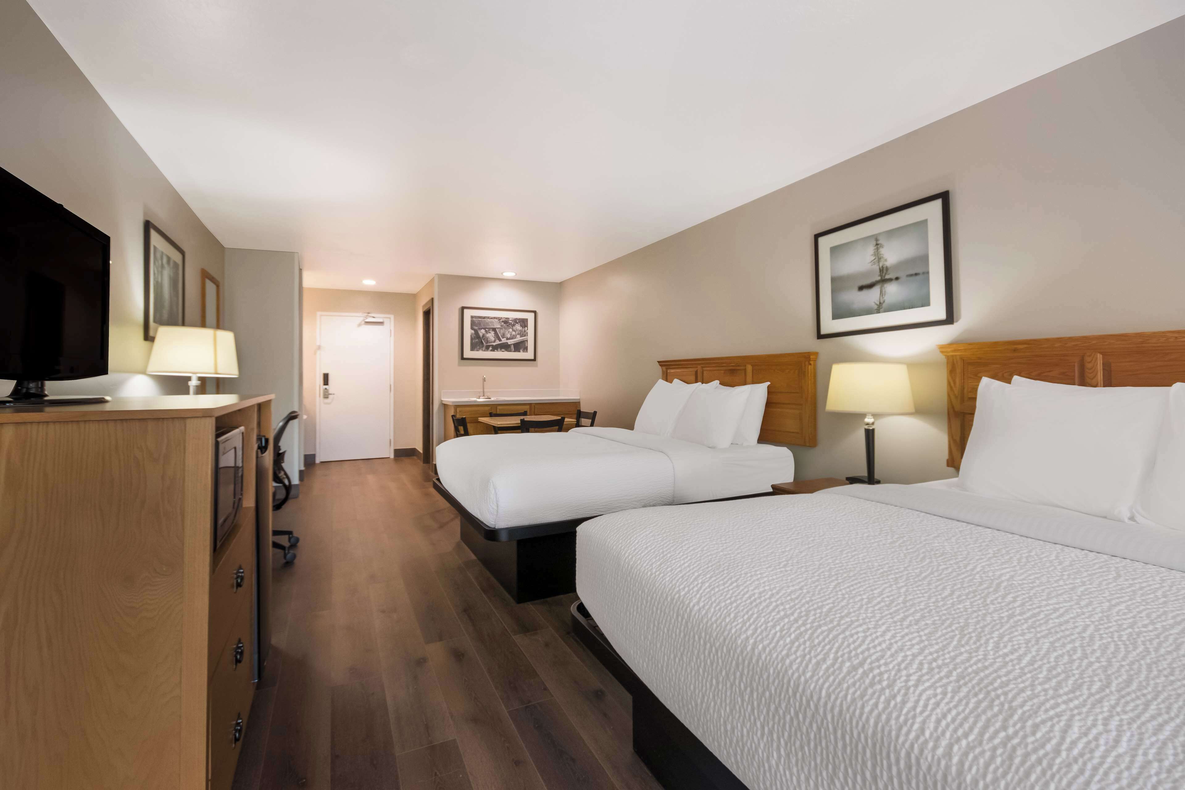 A hotel room with two beds, a desk, a TV, and a door leading to a bathroom.