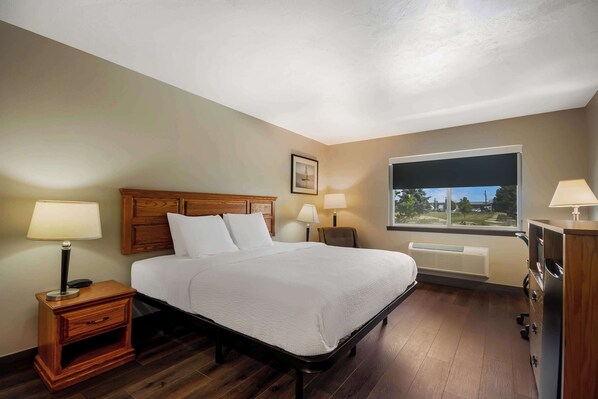 A neatly arranged bedroom with a bed, bedside lamps, a wooden nightstand, a dresser, and a window with a view.