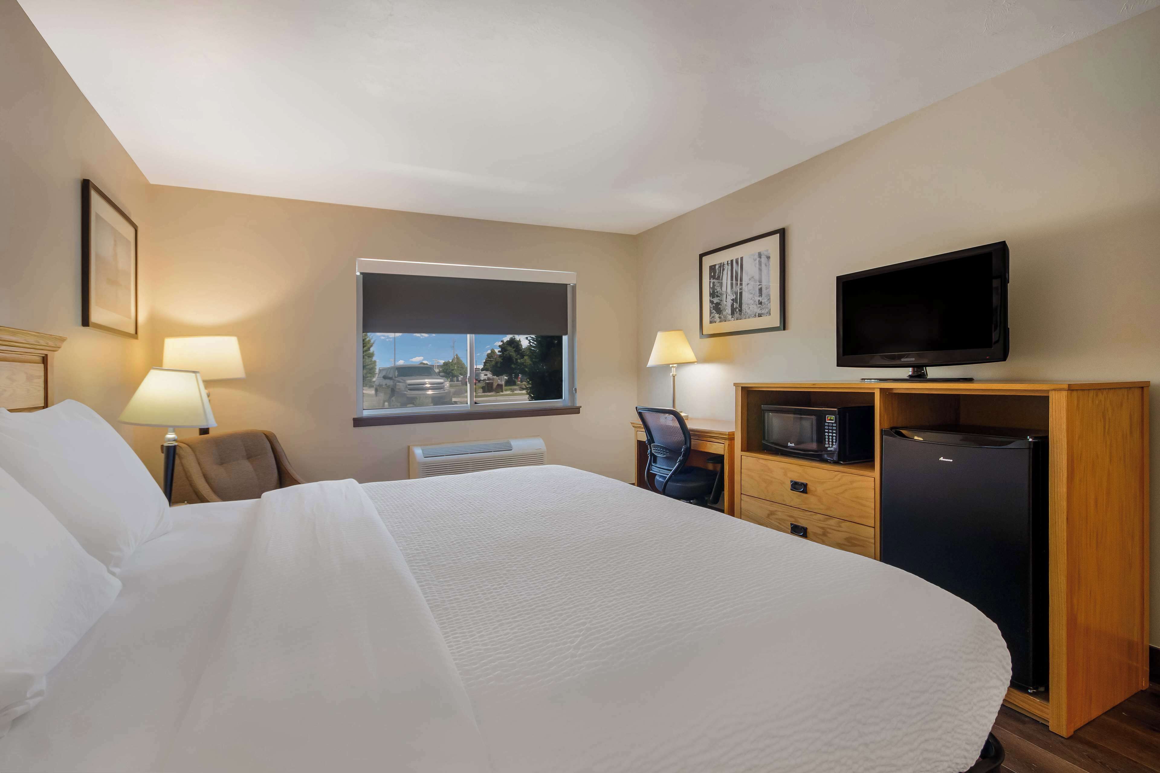 A hotel room with a large bed, a desk with a computer, a television, and a refrigerator.