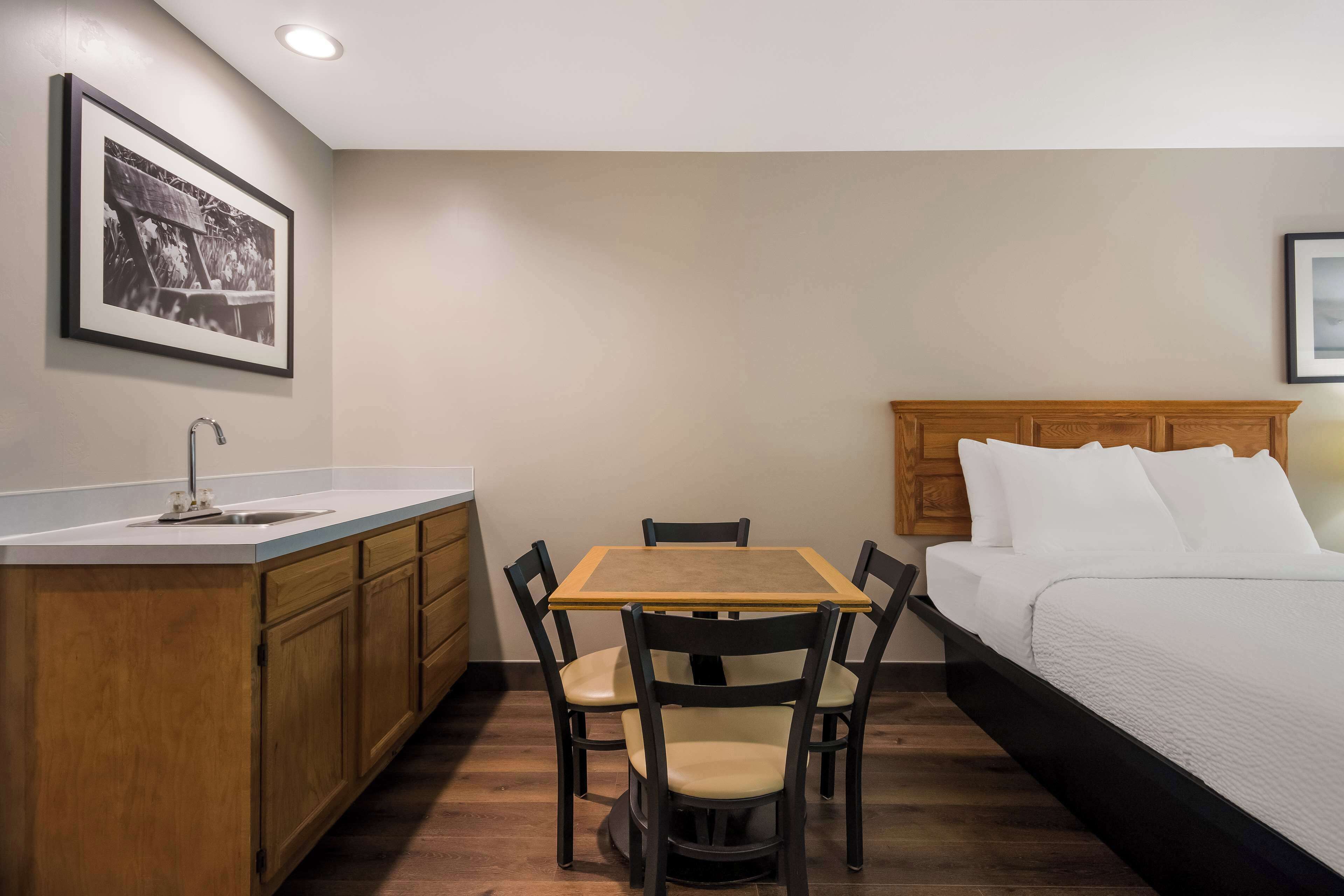 A compact room with a bed, a small table with chairs, a kitchenette, and a framed picture on the wall.