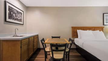 A compact room with a bed, a small table with chairs, a kitchenette, and a framed picture on the wall.