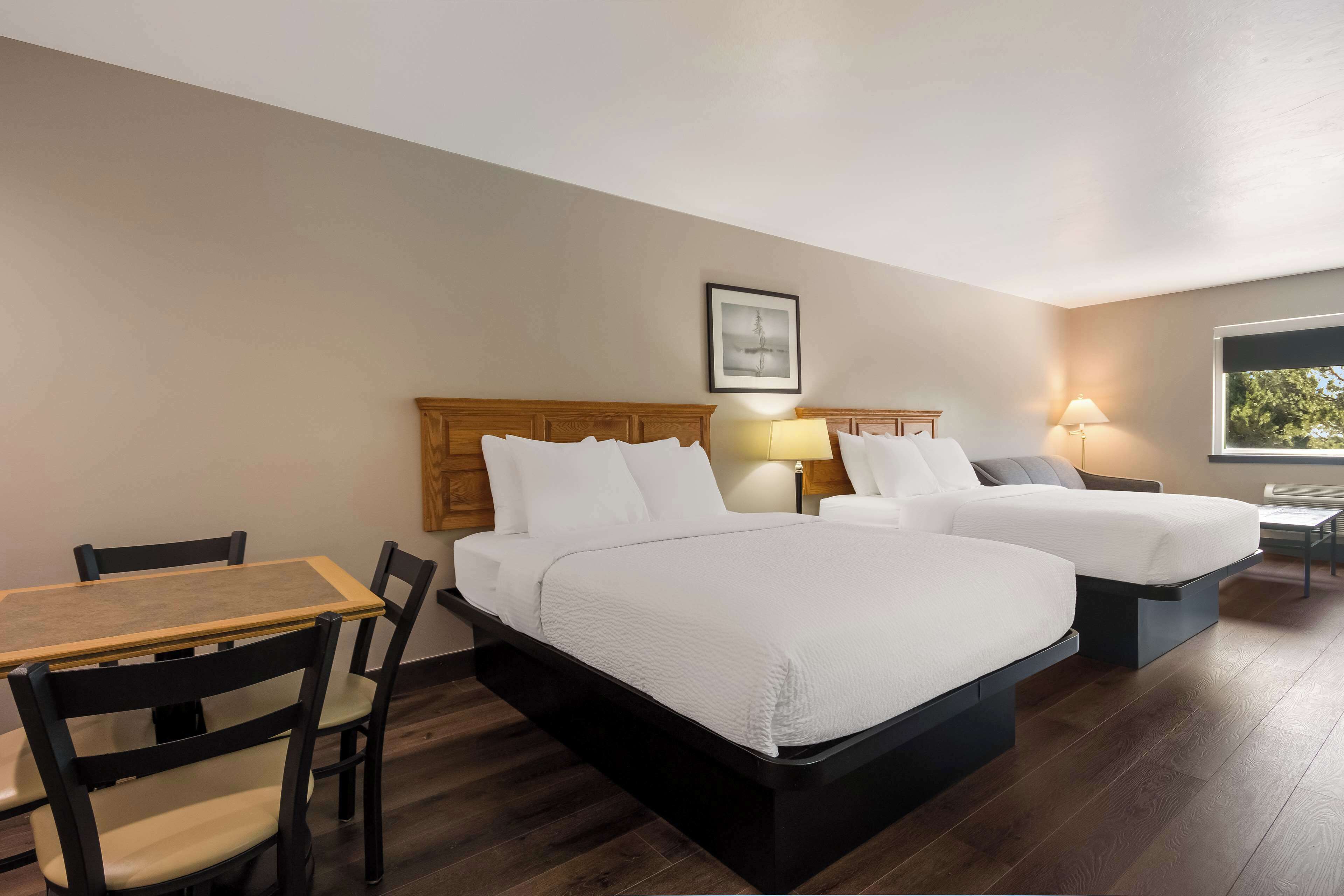 A hotel room with two beds, a wooden table, and chairs.