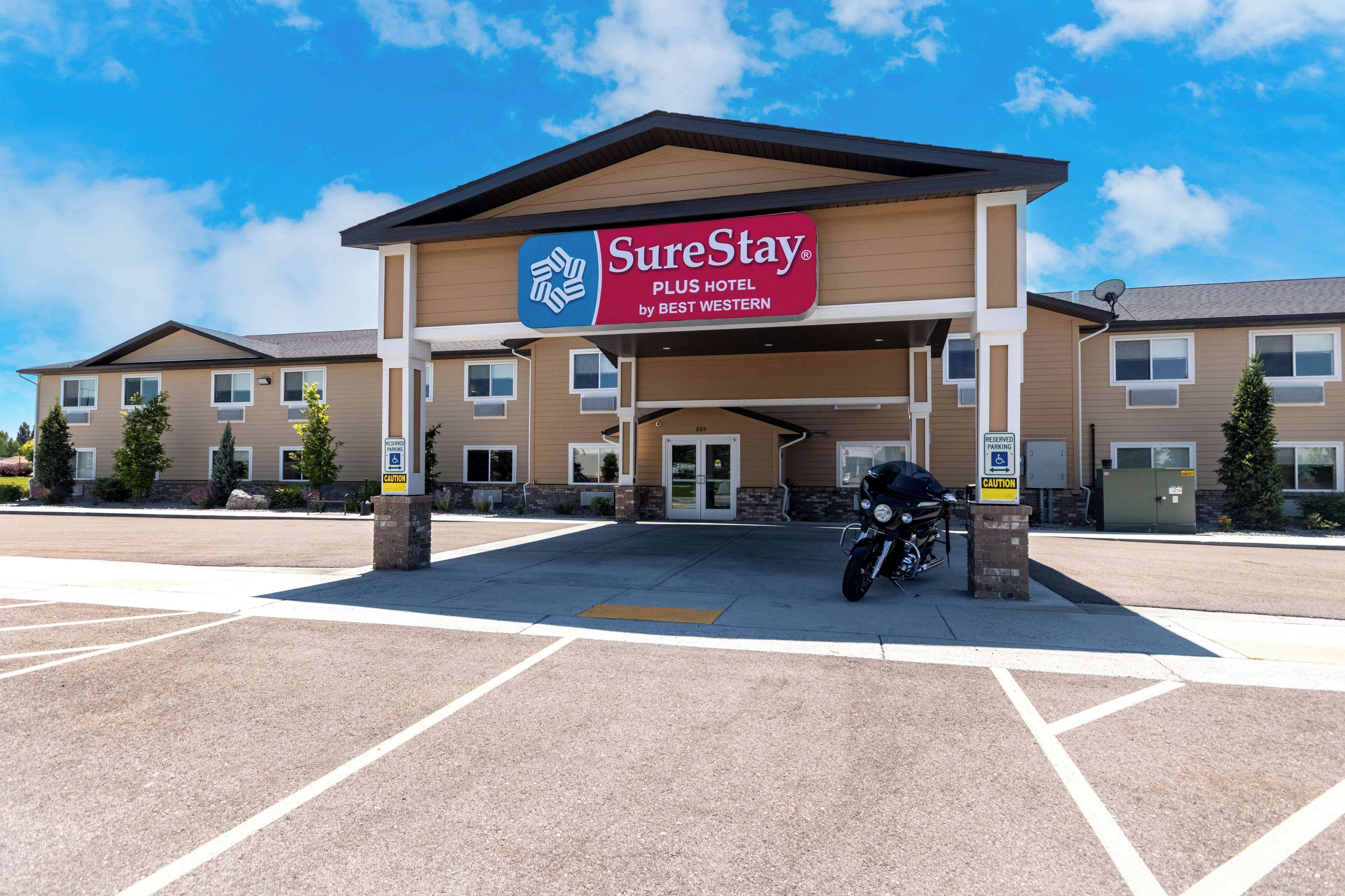 A SureStay Plus Hotel by Best Western with a parking lot and a motorcycle parked in front.