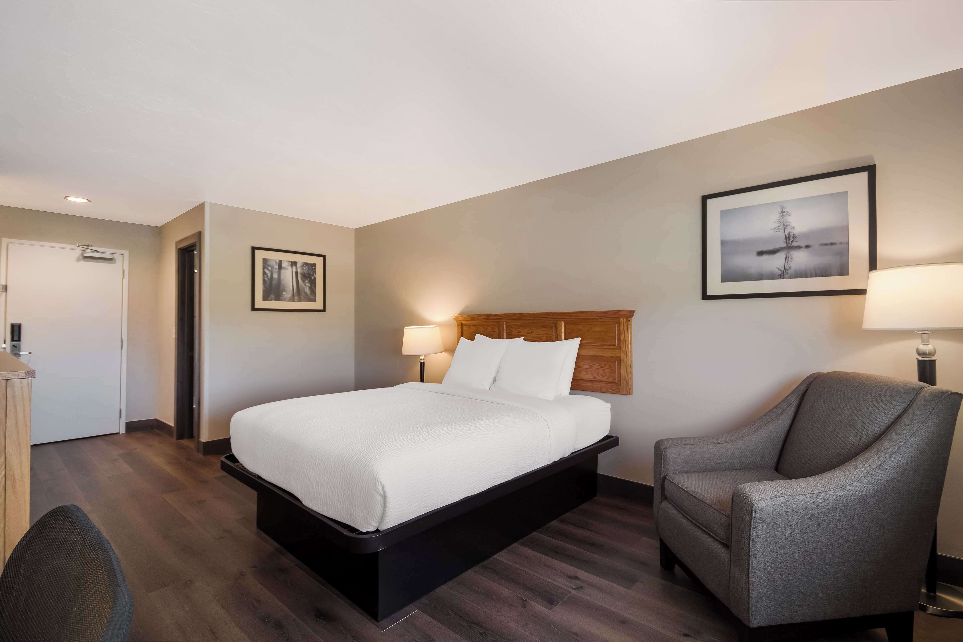 A hotel room with a bed, a chair, a desk, a door, and two wall-mounted lamps.