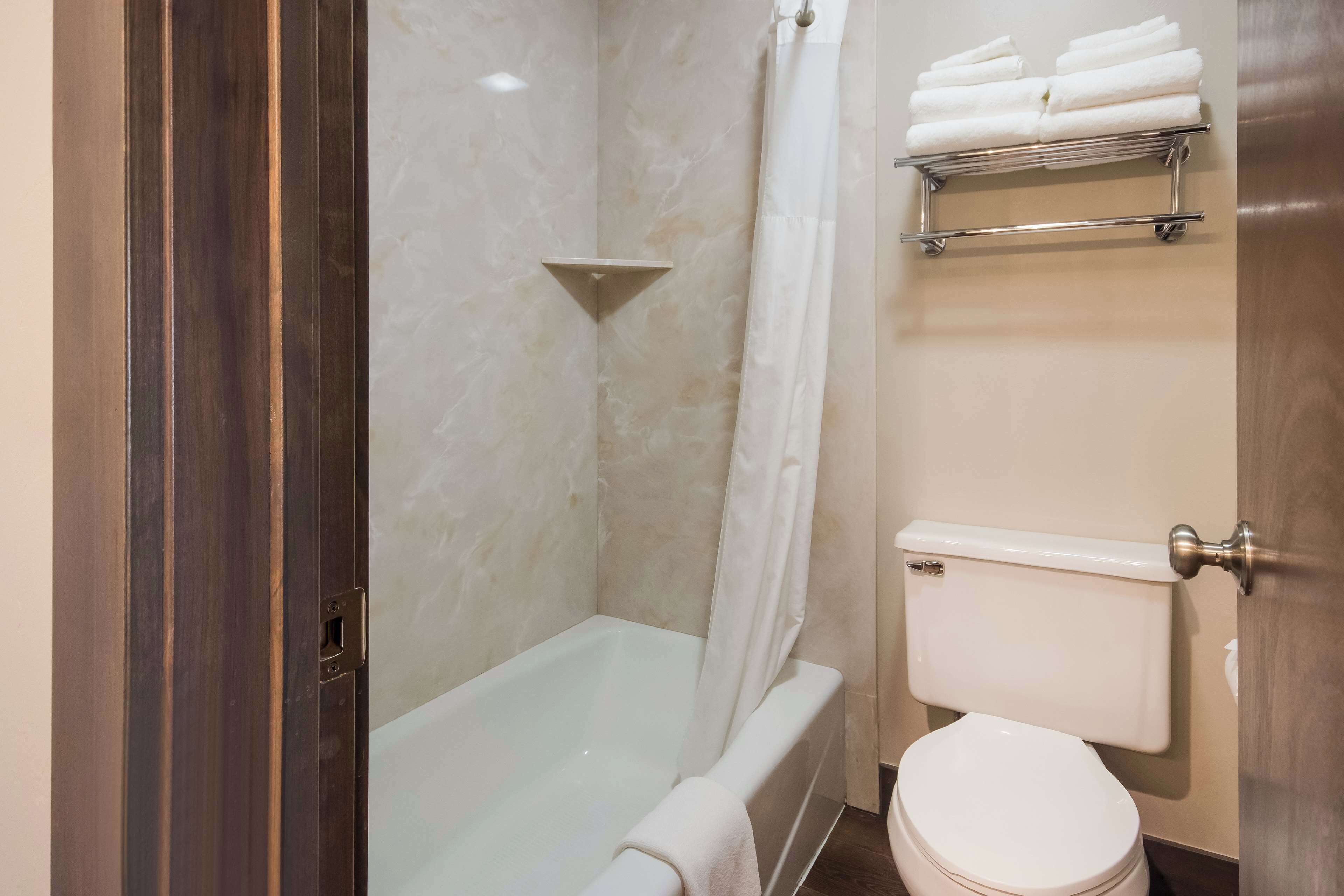 A bathroom with a bathtub, toilet, and a shelf with folded towels.