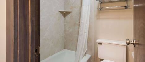 A bathroom with a bathtub, toilet, and a shelf with folded towels.