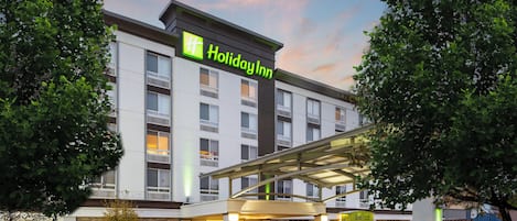 Un hotel Holiday Inn con diseño moderno, que presenta una entrada cubierta y fachada de ladrillo.