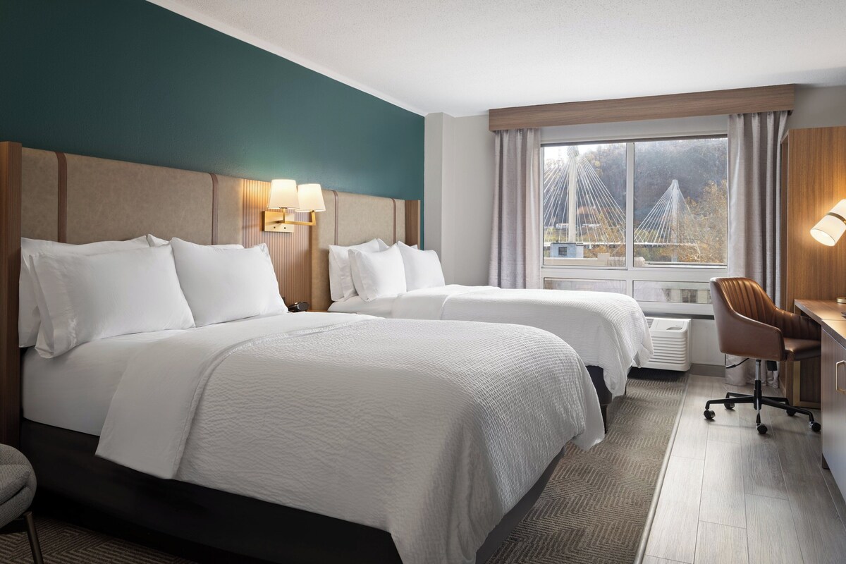 A hotel room with two beds, a desk, and a view of a bridge.