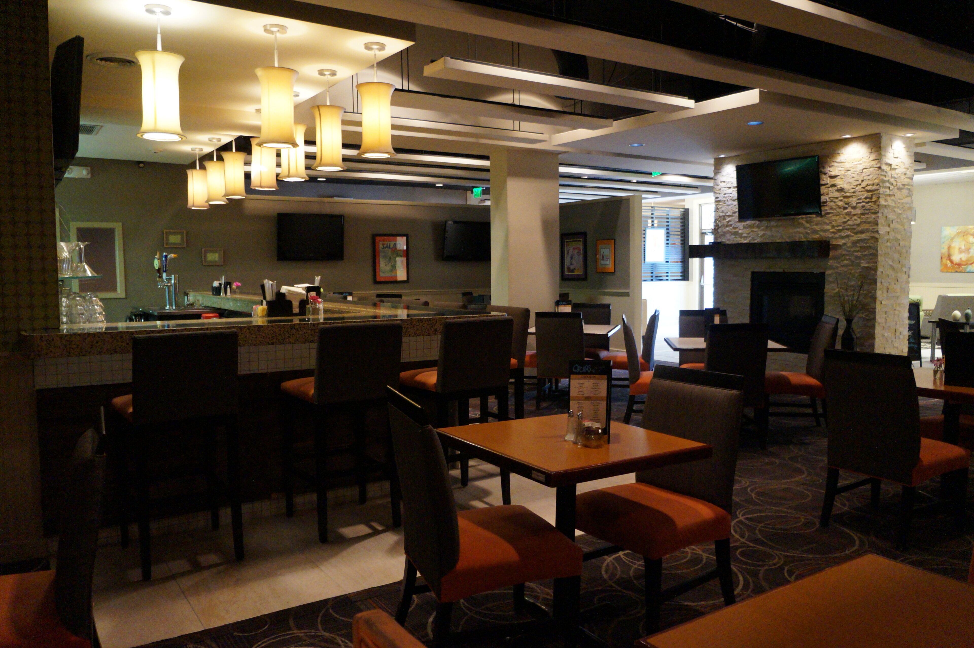 A restaurant interior with multiple tables and chairs, a bar area, and a television mounted on the wall.