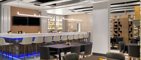 A modern bar area with a long counter, bar stools, and a seating area with tables and chairs.