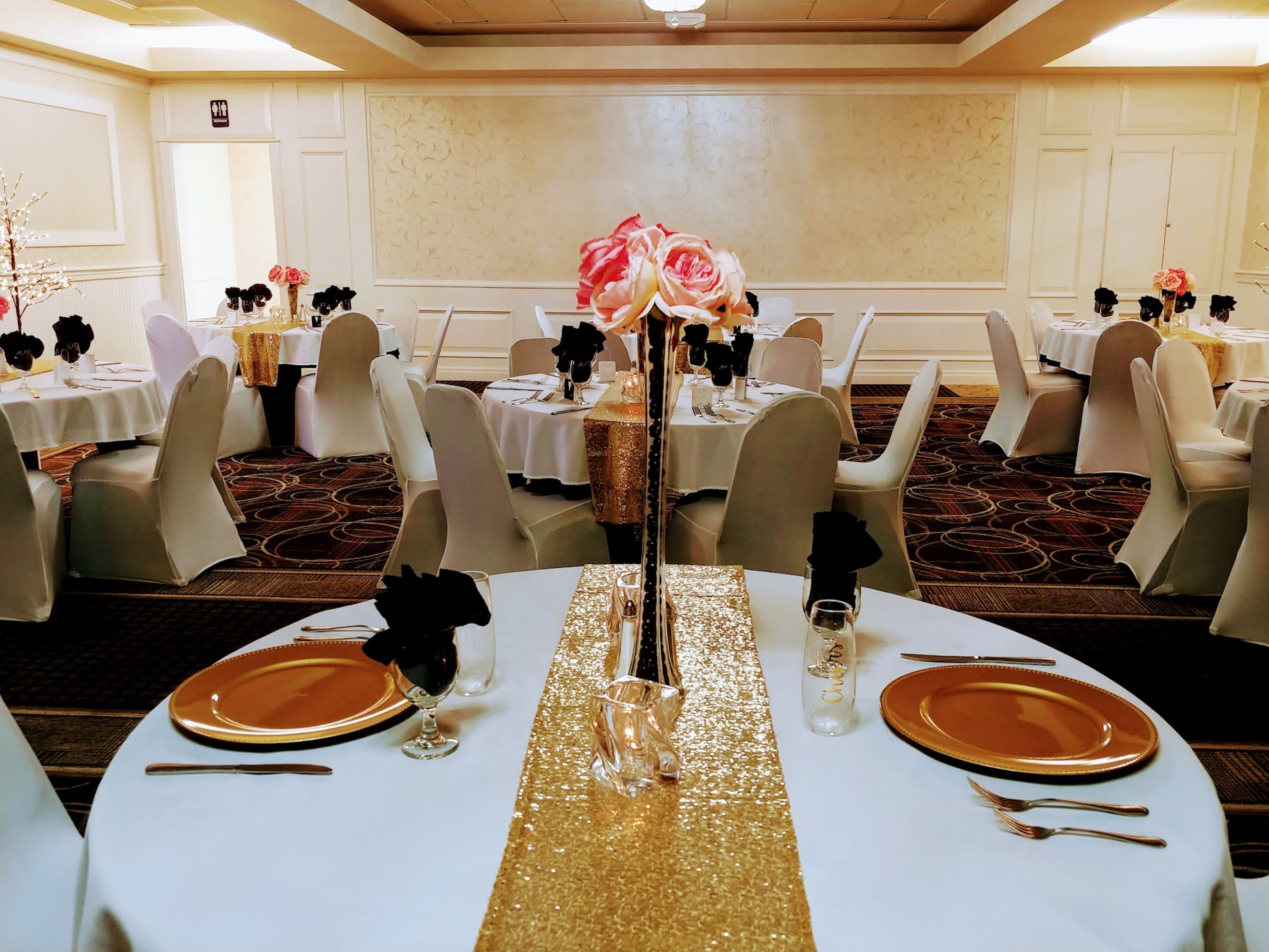 A banquet hall with round tables, white tablecloths, and chairs with white covers.