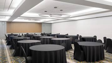 A conference room with multiple round tables, black chairs, and a patterned carpet.