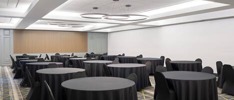 Un salón de conferencias con varias mesas redondas, sillas negras y una alfombra estampada.