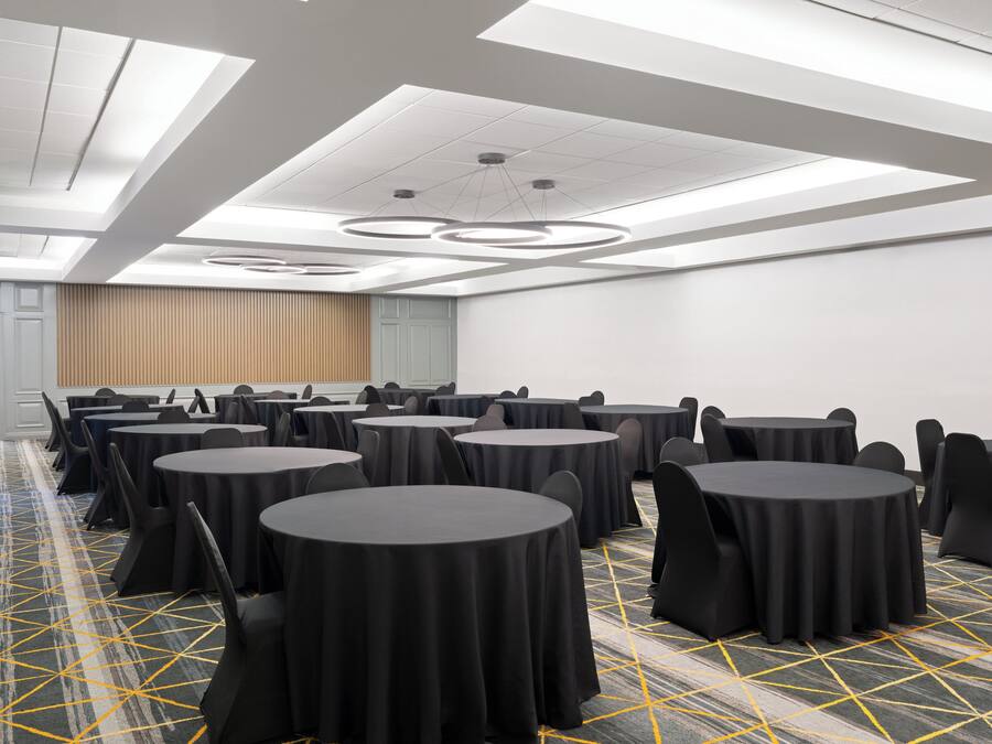 A conference room with multiple round tables, black chairs, and a patterned carpet.