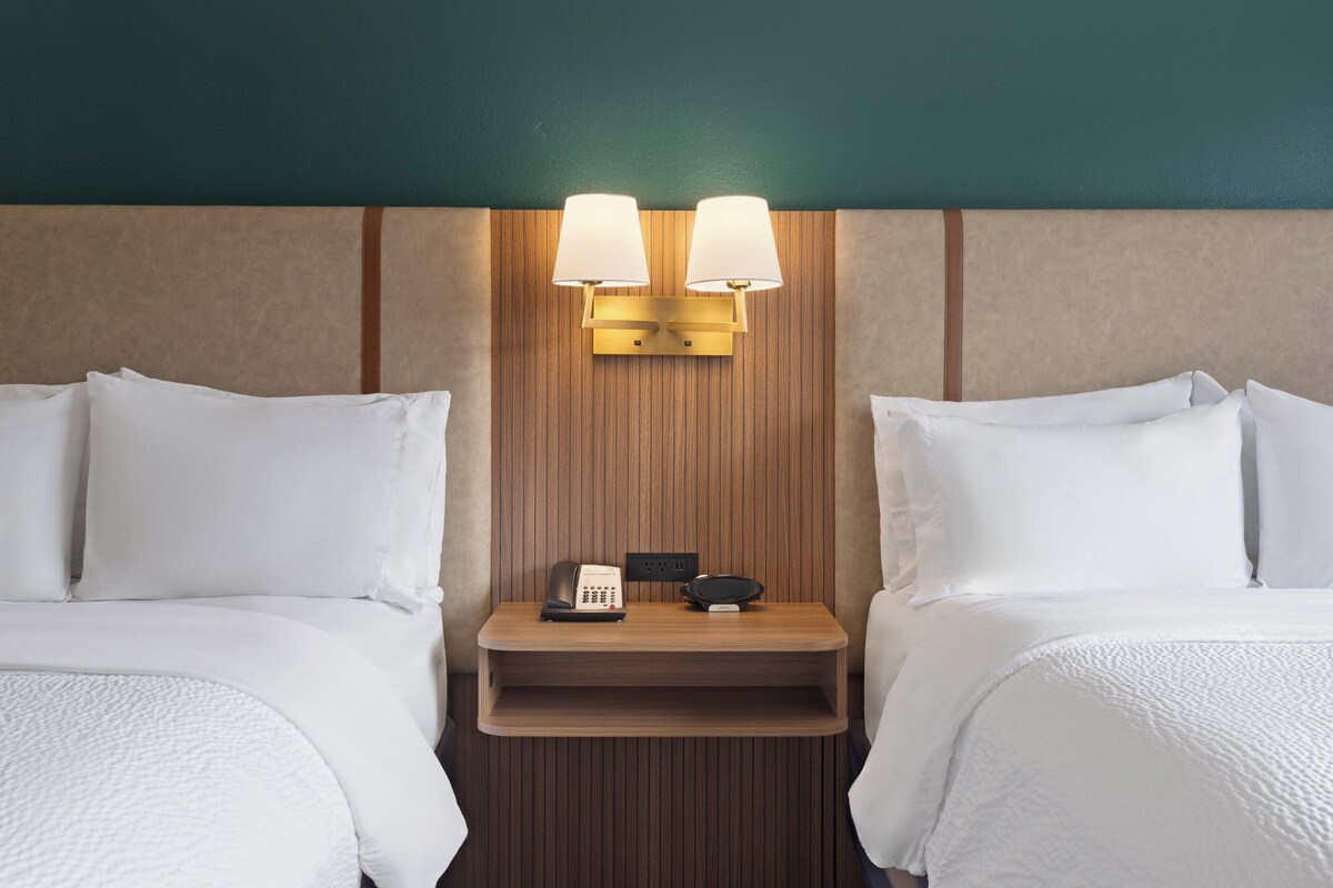 A hotel room with two beds, a wooden headboard, a nightstand with a lamp, and a telephone.