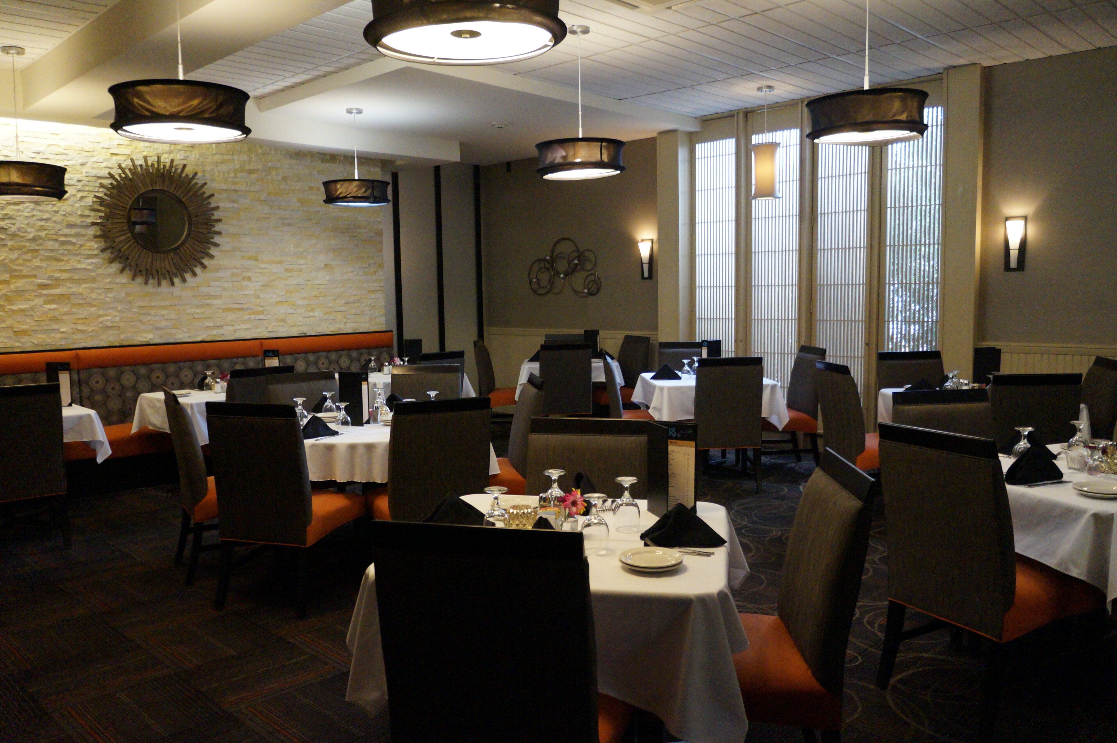 A restaurant with multiple tables and chairs, a stone wall with a sunburst mirror, and pendant lighting.