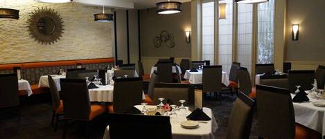 A restaurant with multiple tables and chairs, a stone wall with a sunburst mirror, and pendant lighting.