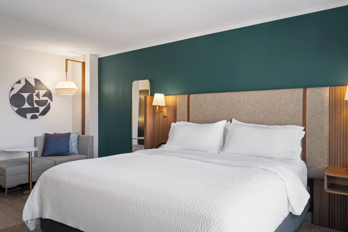 Ein Hotelzimmer mit einem großen Bett, einem kleinen Tisch, einer Couch und einem Spiegel.