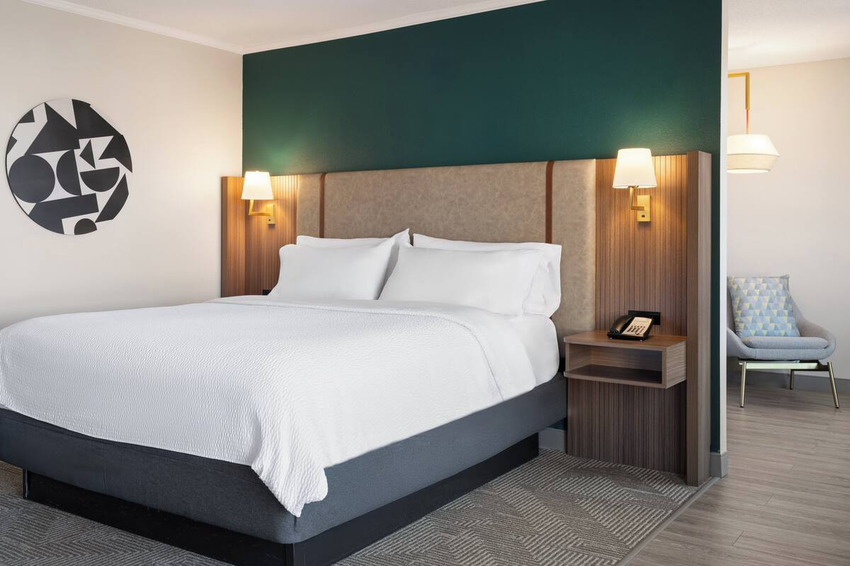 Ein modernes Hotelzimmer mit einem großen Bett, zwei Nachttischlampen, einem Sessel und einem Wandbild.