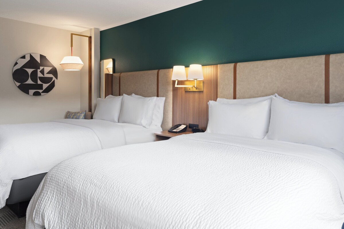 A hotel room with two beds, a round wall art piece, and a nightstand with a phone and lamp.
