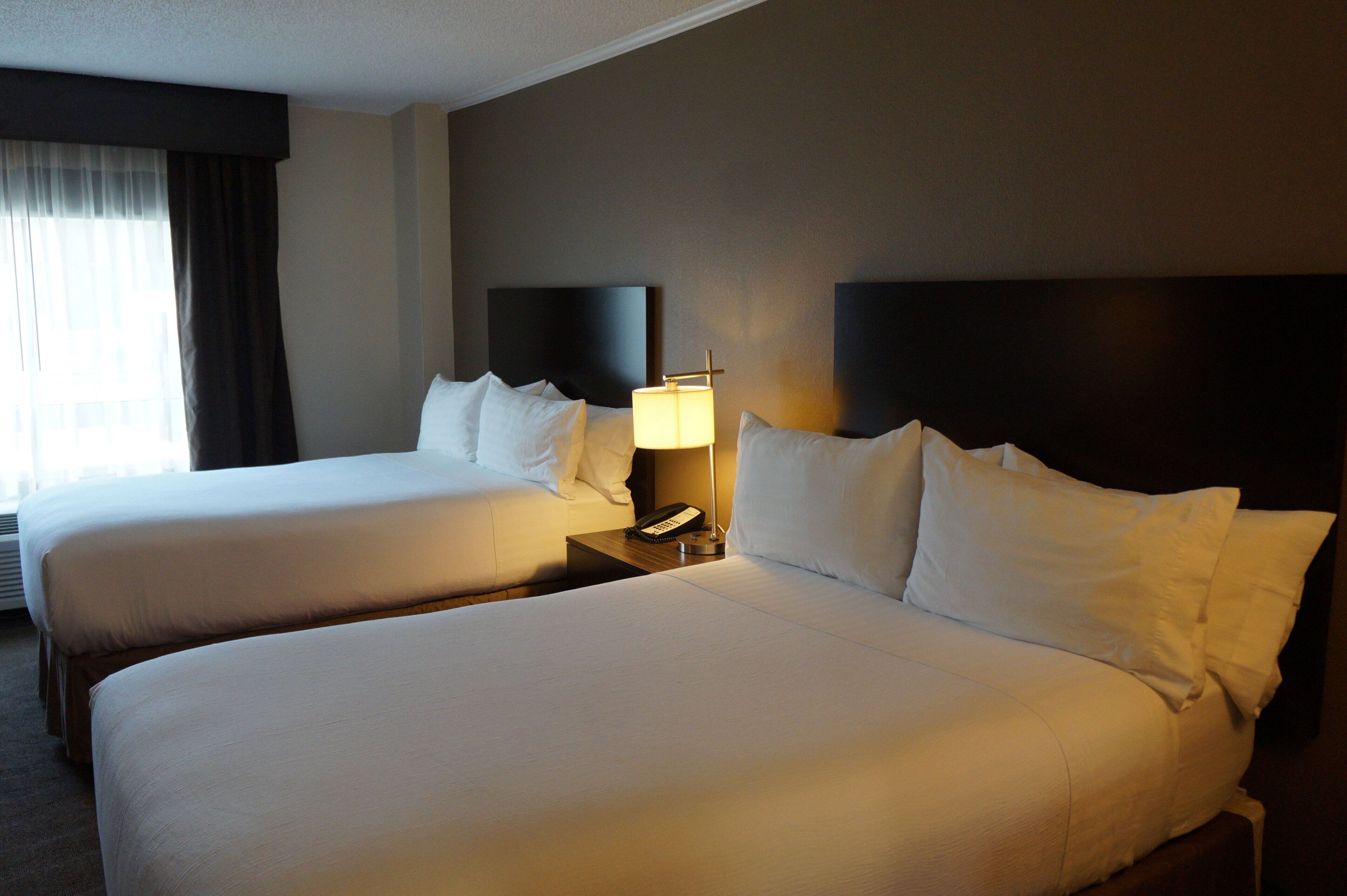 A hotel room with two beds, a nightstand with a lamp, and a window with curtains.