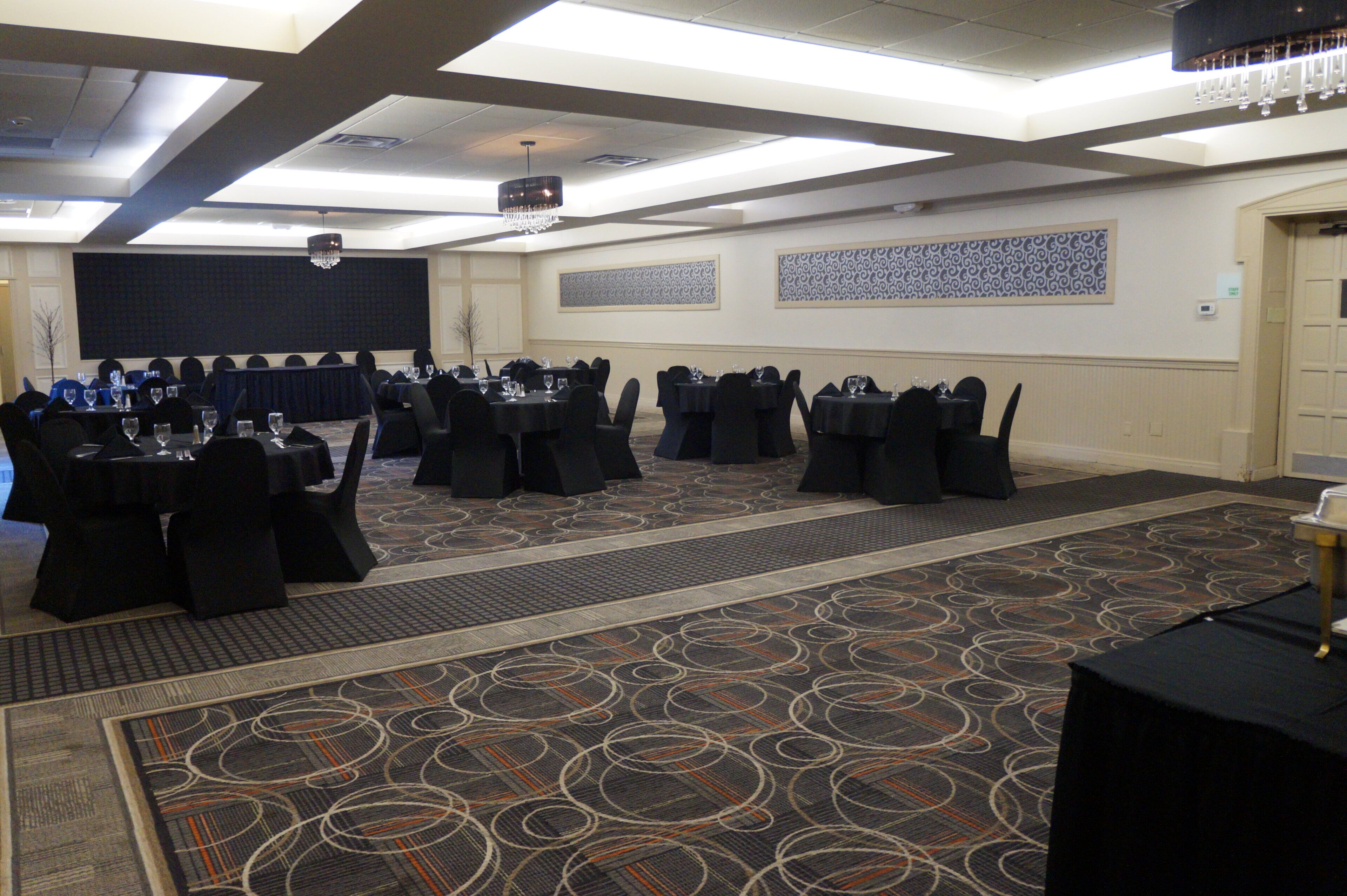 Un salón de conferencias con varias mesas y sillas, una alfombra estampada y un candelabro.