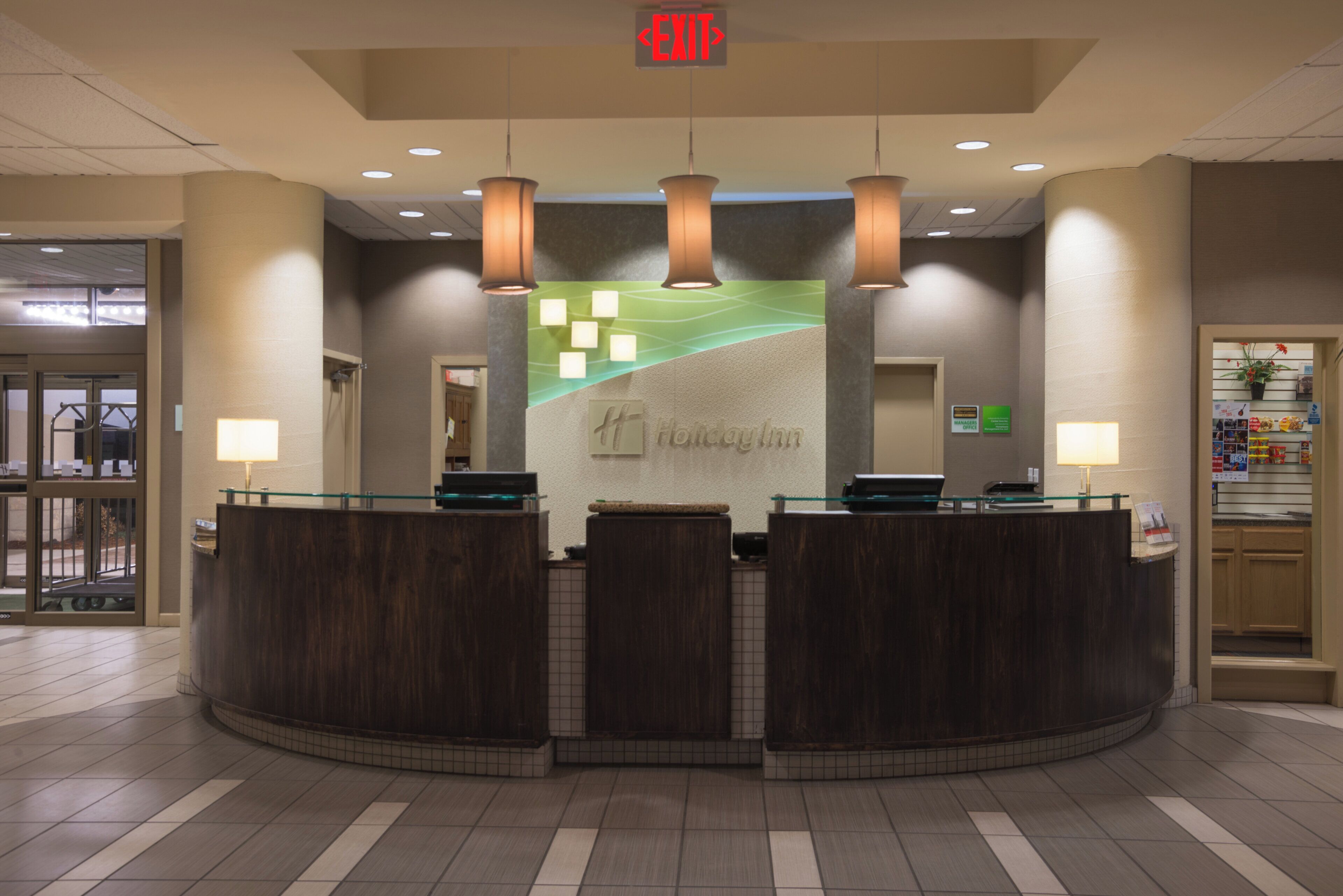 A hotel reception desk with a curved design, a green wall with a wave pattern, and a sign that reads 'Holiday Inn'.