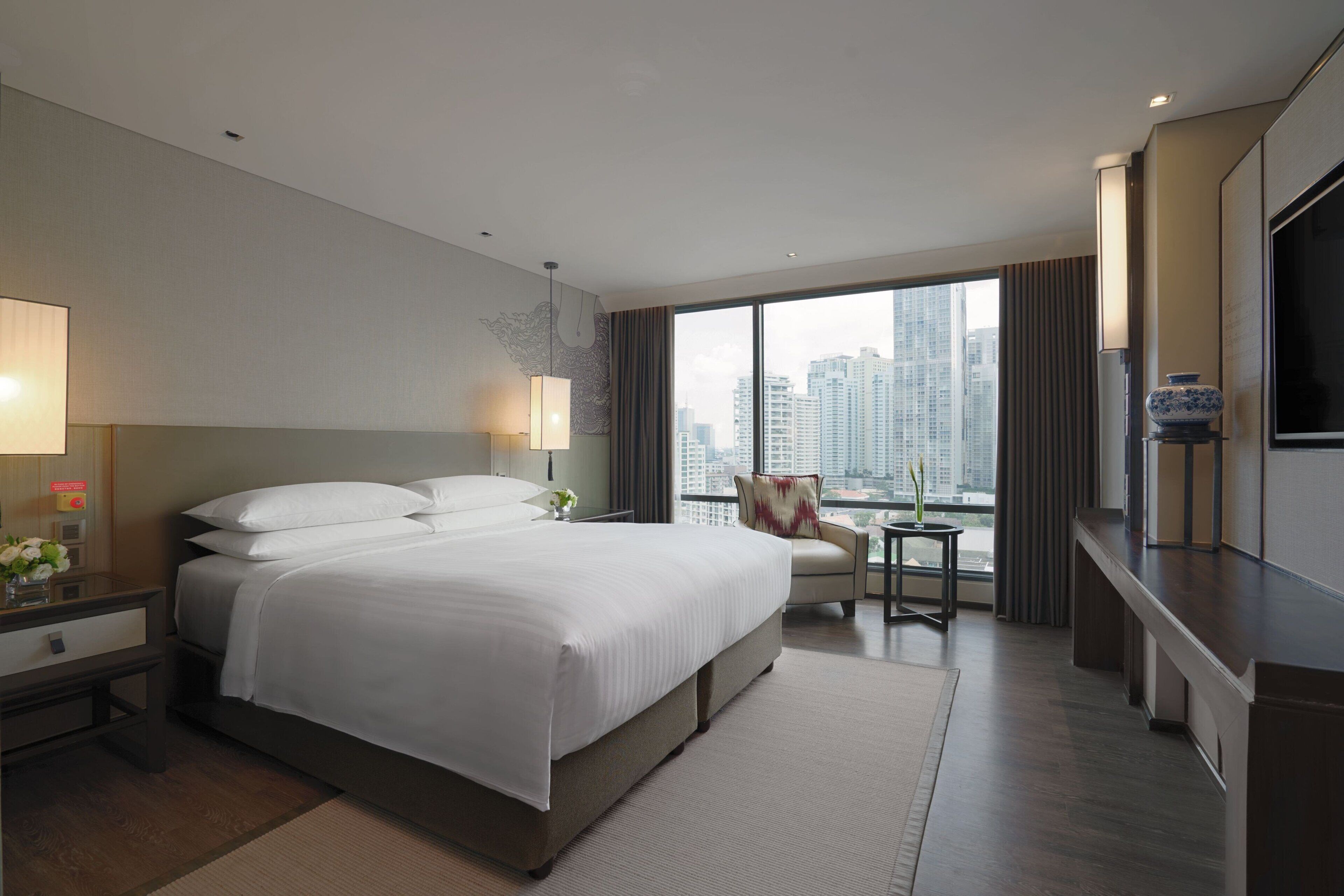 A modern hotel room with a large bed, a desk, a chair, and a TV.