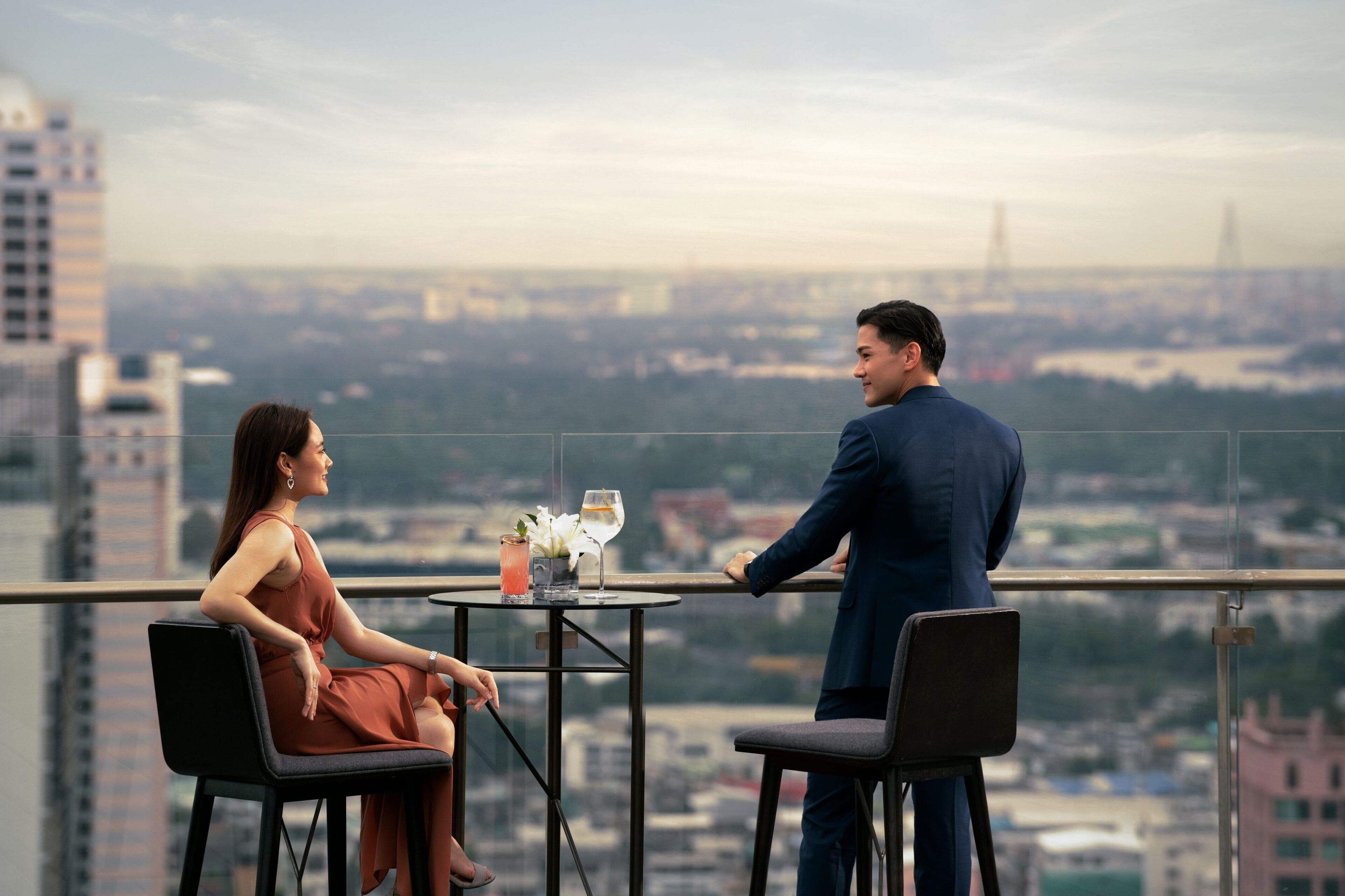 A couple seated at a table with a city view, overlooking buildings and a bridge.