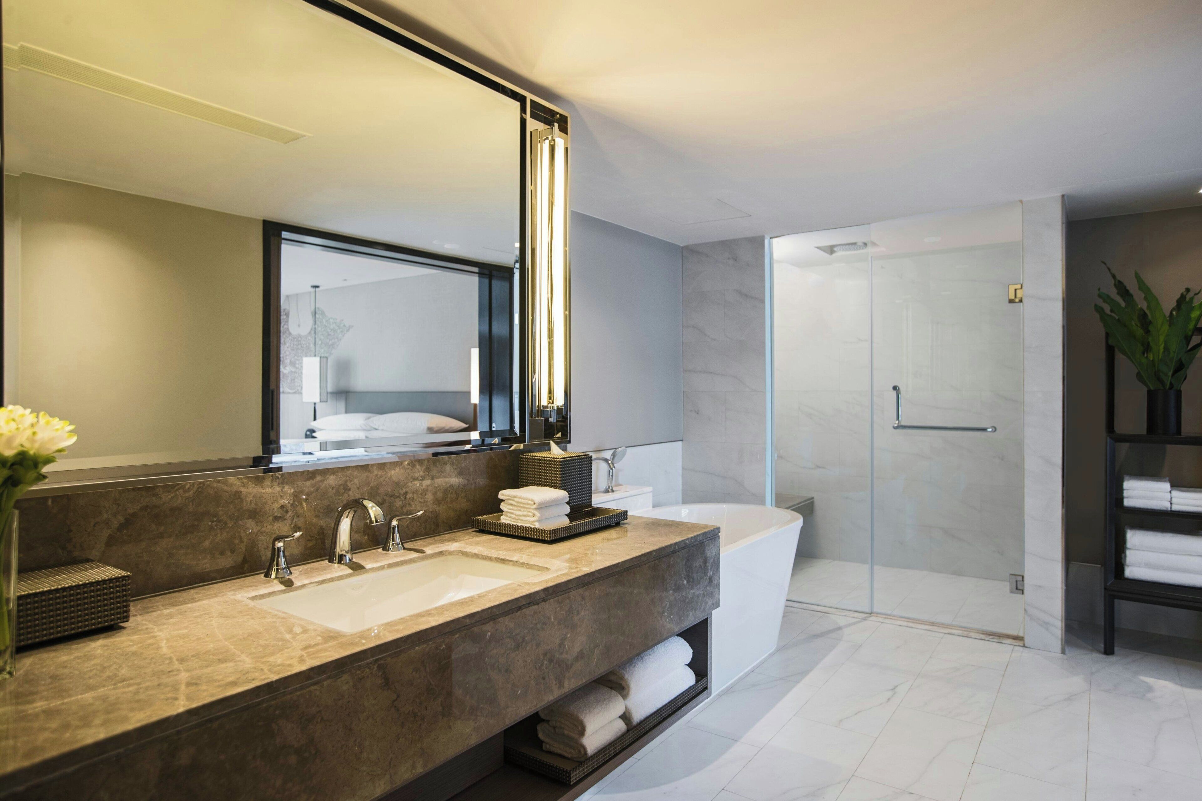 A modern bathroom with a large mirror, two sinks, a bathtub, and a walk-in shower.