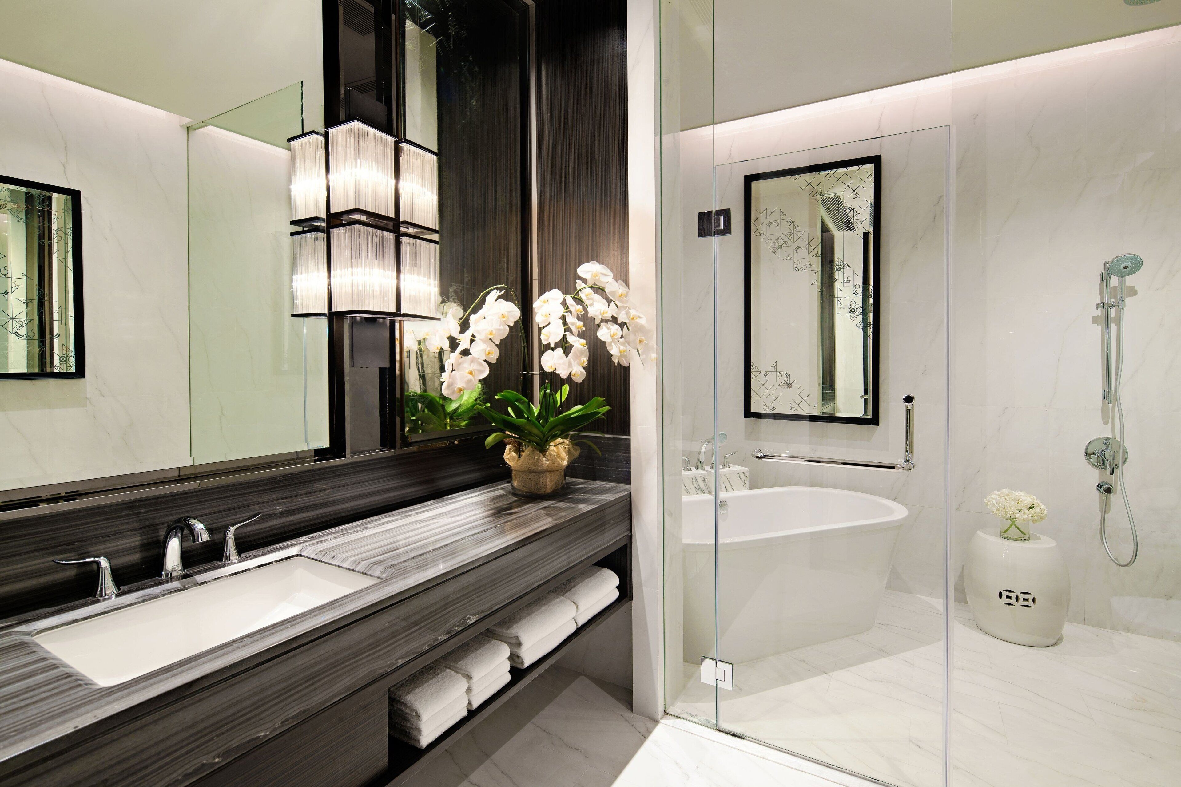 A modern bathroom with a large mirror, a glass-enclosed shower, and a marble countertop.