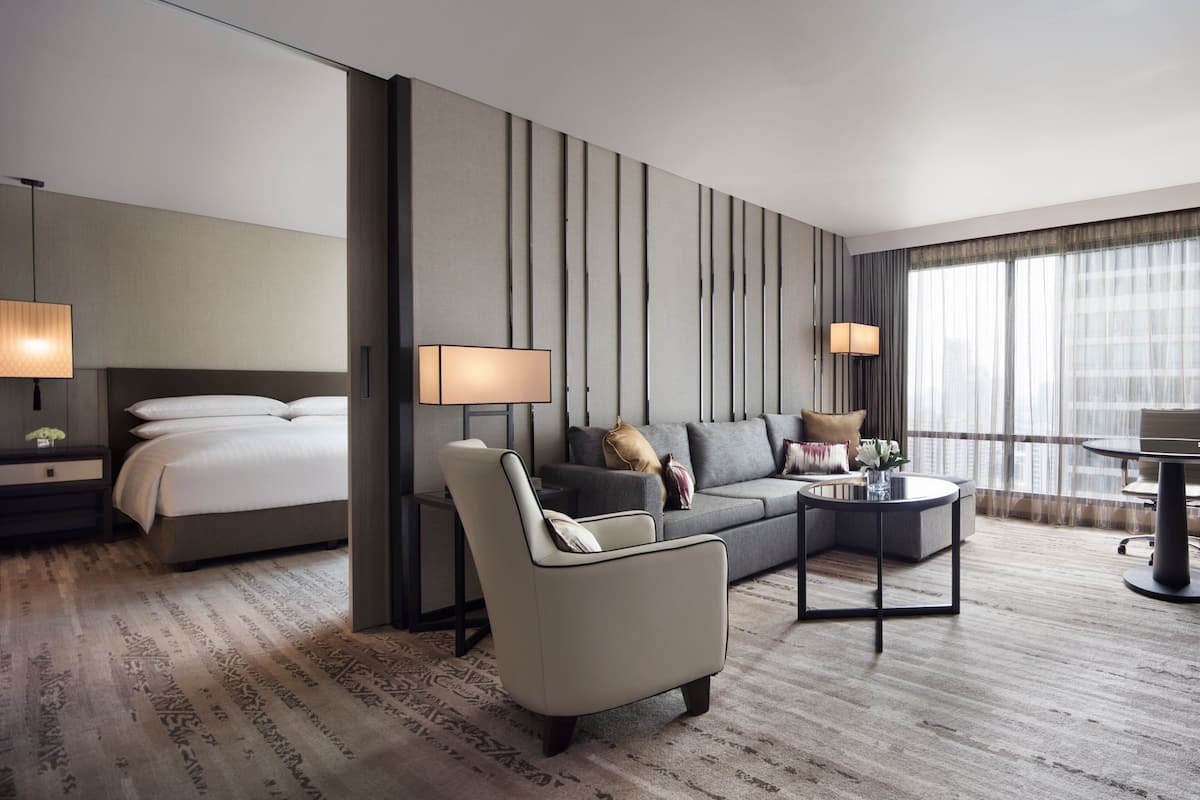A modern hotel room with a bed, a sofa, a coffee table, and a desk.