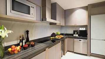 A modern kitchen with a microwave, oven, and dishwasher. There are fruits and vegetables on the counter, and a vase with flowers.