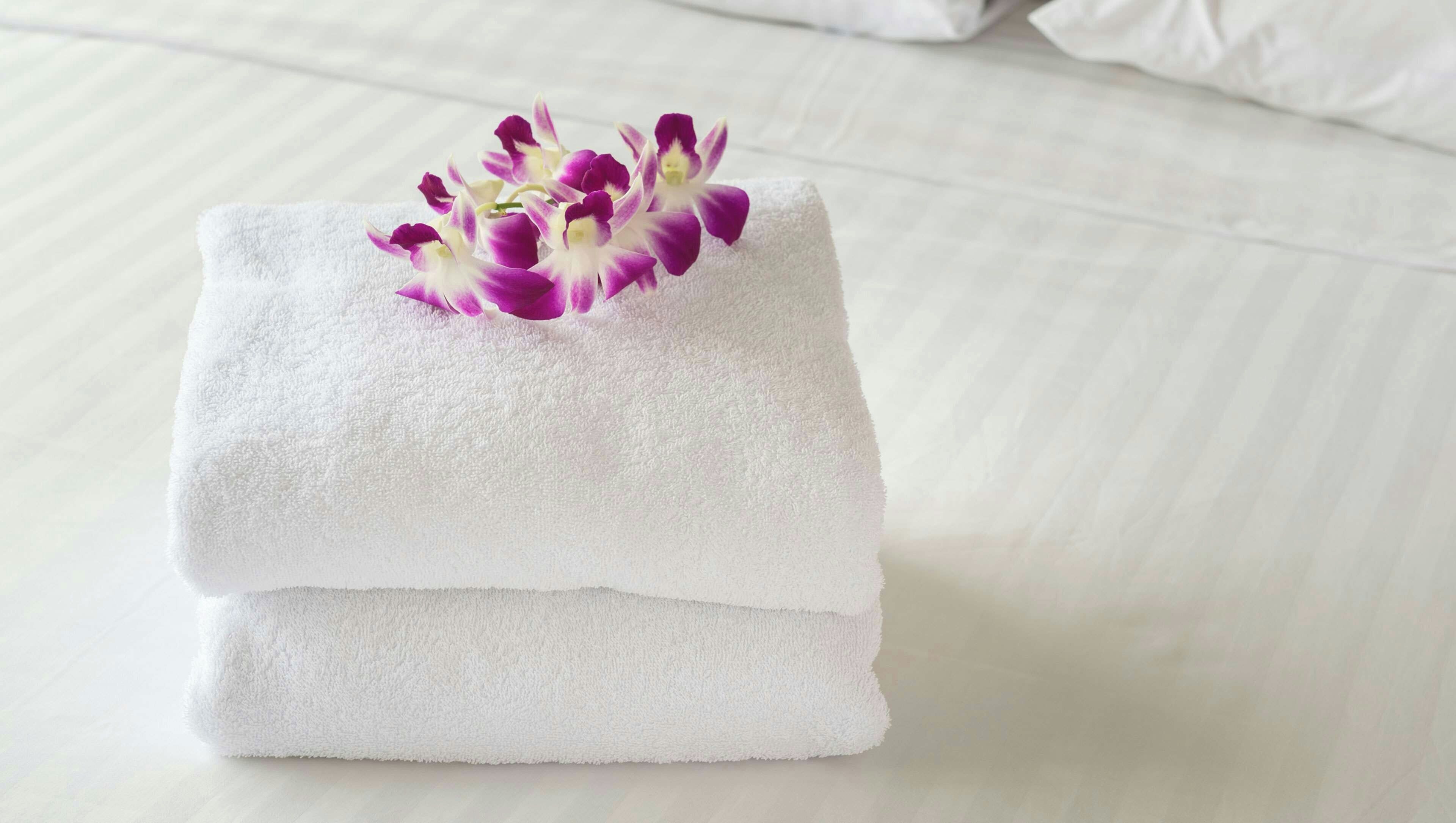 A neatly folded white towel with purple and white flowers on a bed.