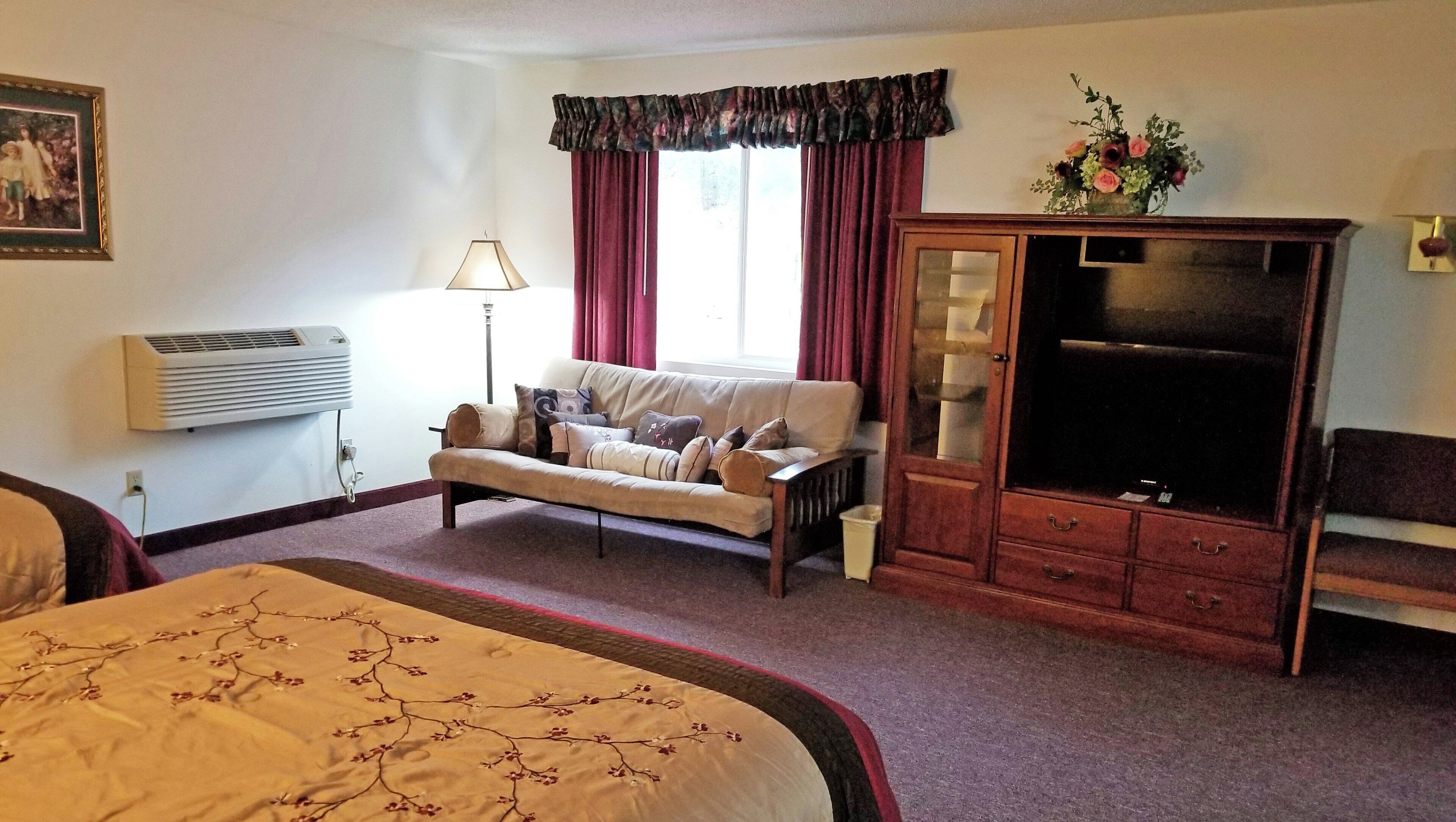 A hotel room with a bed, a sofa, a TV cabinet, and a window with curtains.