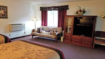 A hotel room with a bed, a sofa, a TV cabinet, and a window with curtains.