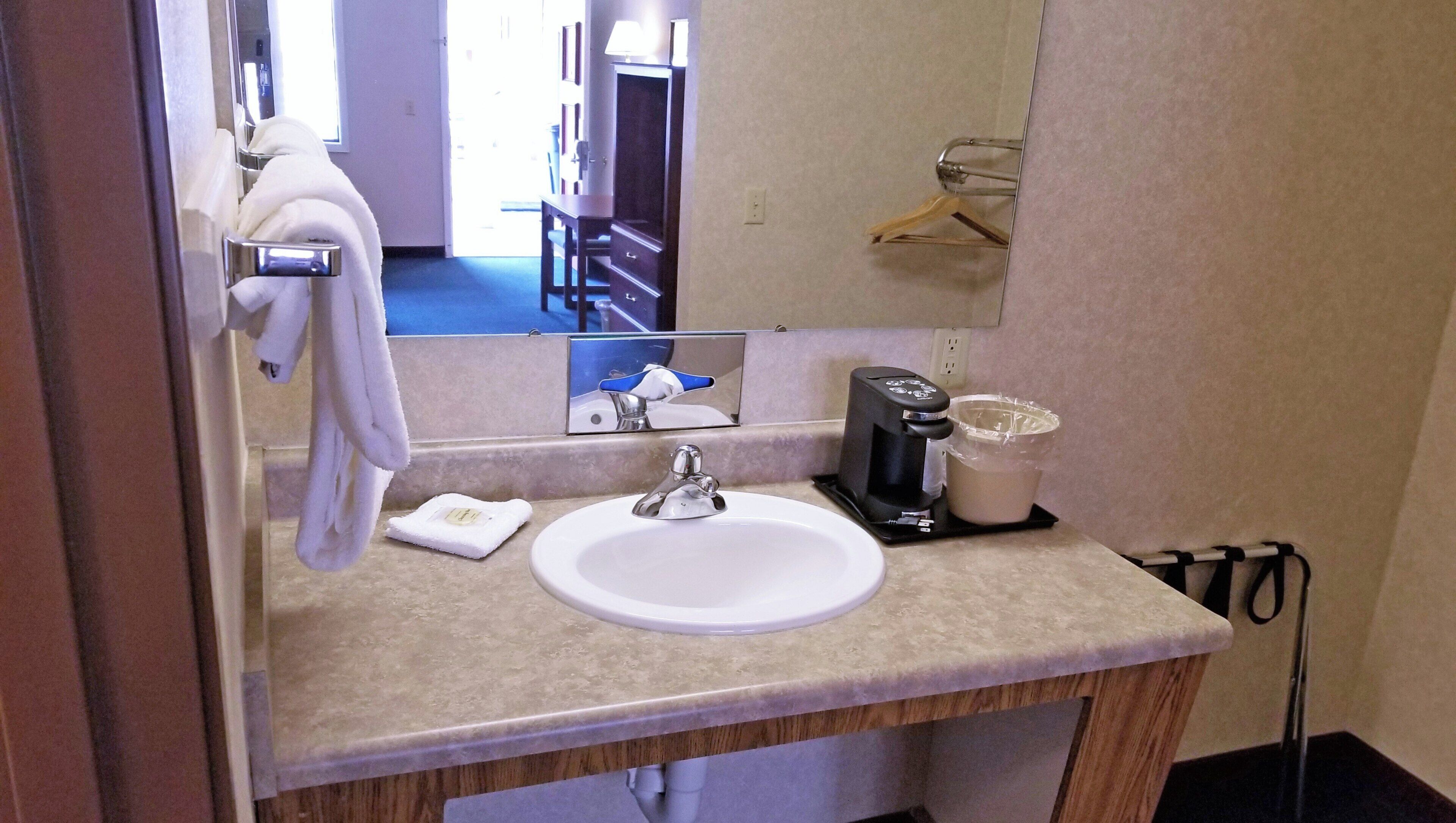A bathroom with a sink, mirror, towel rack, and a coffee maker.