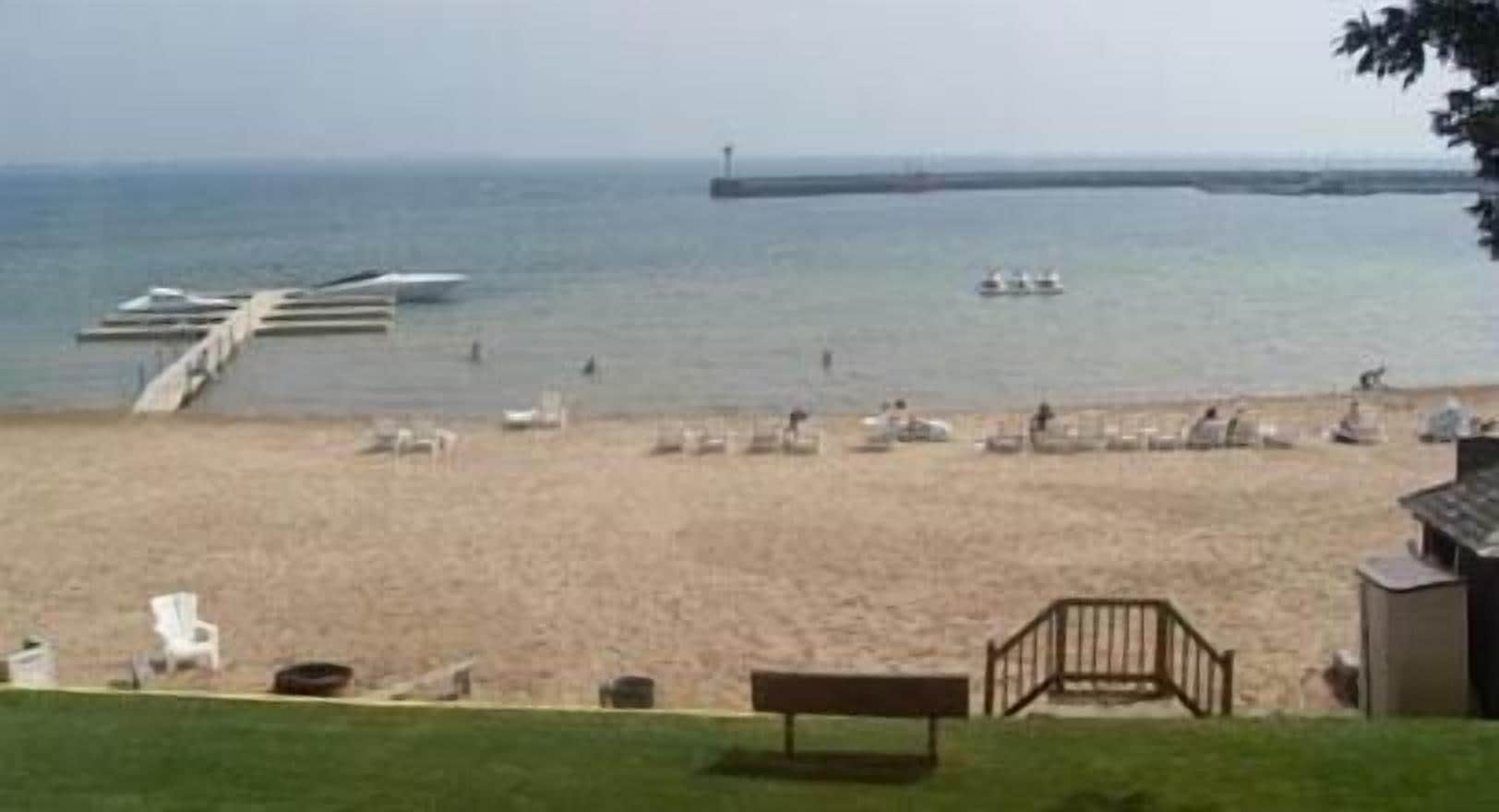 A beach with a pier extending into the water, several boats, and a lighthouse in the distance.